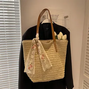 Detail of straw tote bag with brown leather handles and floral embroidery lace scarf
