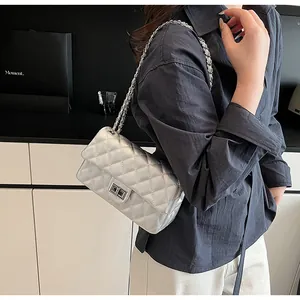 Detail of silver quilted crossbody bag with metal twist lock and chain strap on shoulder