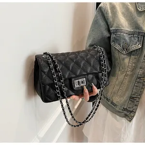 Detail of black quilted leather shoulder bag with silver chain strap and square metal lock