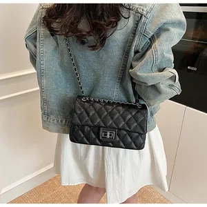 Detailed view of black quilted crossbody bag with silver rotating clasp on denim jacket