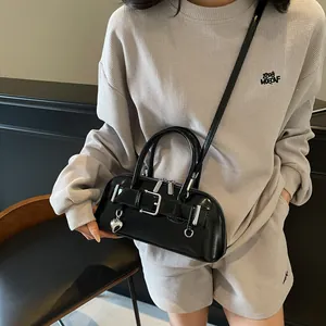 Sac baguette noir brillant avec boucle argentée et breloque cœur porté à l'épaule