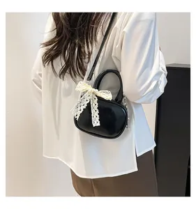 Close-up of black patent leather crossbody bag with a white lace bow on female model