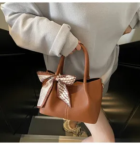 Détail d'un sac seau en cuir marron à motif litchi avec un foulard fleuri sur l'anse