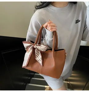Détail du sac seau en cuir grainé marron avec foulard décoratif en soie sur la poignée