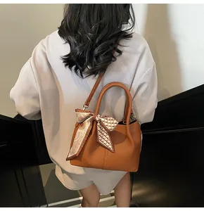 Détail du sac seau en cuir marron avec foulard floral décoratif et bandoulière amovible