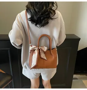 Détail du sac seau en cuir marron avec foulard décoratif en soie fleurie sur la poignée