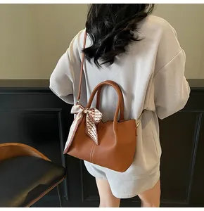 Détail du sac à main marron en cuir grainé avec foulard en soie et finitions dorées