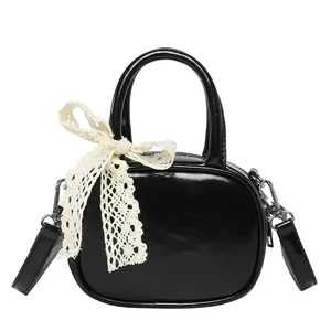 Glossy black mini handbag with a cream lace bow accent and adjustable shoulder strap