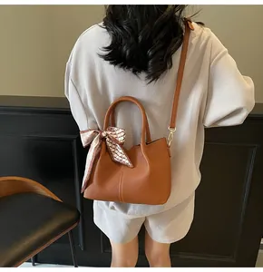 Sac seau marron grainé avec accessoire en soie sur la bandoulière porté par un mannequin