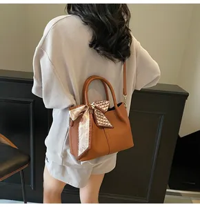 Détail du sac seau en cuir marron grainé avec foulard en soie floral décoratif au manche