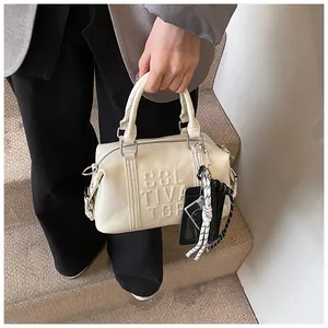 Chic cream Boston bag with embossed CULTIVATOR text and stylish woven rope pendant