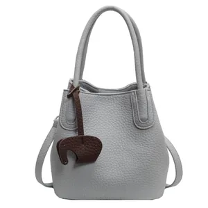 Detail of light gray lychee grain leather bucket bag with cute elephant charm