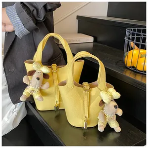 Detailed view of yellow litchi grain bucket bags with lock and plush puppy charms