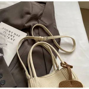 Close-up of beige lychee texture leather bucket bag with leaf charm on blazer background