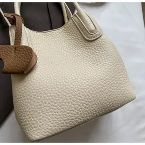 Close-up of creamy white lychee grain leather bucket bag with a brown charm detail