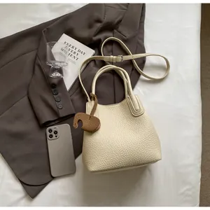 Flat lay of cream lychee texture bucket bag with adjustable strap and elephant charm
