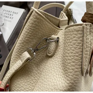 Detailed macro view of litchi grain cream bucket bag with silver metal strap hardware