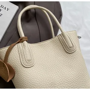 Detail of off-white lychee texture leather tote bag with a dark brown teardrop charm