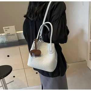 Detail of white lychee leather bucket bag featuring a cute brown elephant charm