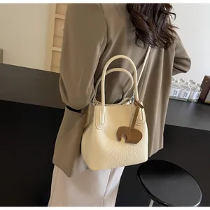 Detail of cream-colored bucket bag with litchi texture and elephant leather pendant