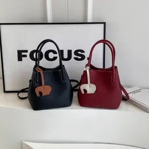 Minimalist litchi grain leather bucket bags in black and burgundy with elephant charms