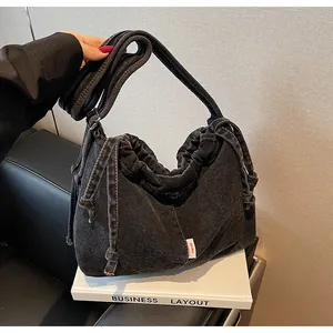 Détail du sac cabas en jean noir avec plis coulissants et étiquette rouge latérale