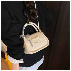 Detail of cream crossbody bag with lace trim and elegant bow accent on model