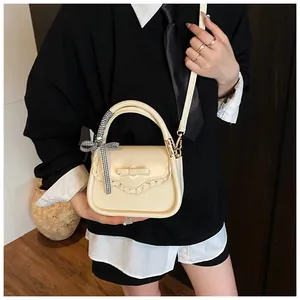 Detail of cream crossbody bag with 3D bow, lace edges, and checkered ribbon handle