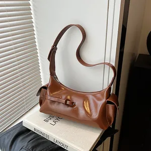 Sac sous le bras marron brillant avec boucles décoratives et poches latérales sur livre