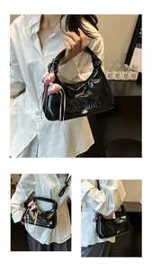 Détail du sac hobo noir brillant avec logo embossé et un nœud en satin rose décoratif