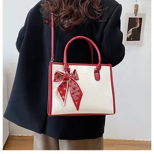 Détail du sac à main bicolore avec poignée rouge et foulard en soie sur un mannequin