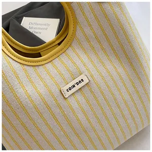 Detailed close-up of striped canvas tote with yellow leather handles and sewn logo tag