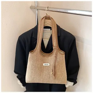 Detail of beige straw tote bag with brown leather handles and a fringe charm detail