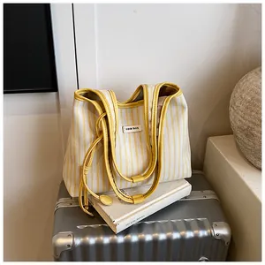 Detailed shot of yellow striped canvas tote bag with reinforced handles on a suitcase