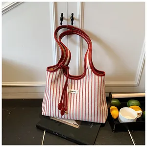 Close-up of red striped canvas tote bag with leather straps and logo label on books