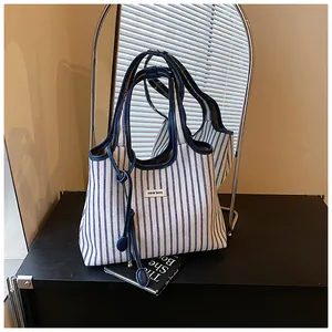 Close-up of a striped canvas tote bag with leather handles and a woven CON'DNE logo patch