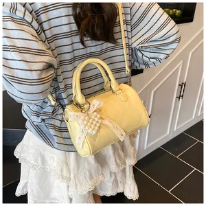 Close-up of yellow Boston bag with pearl heart charm and delicate lace bow detail