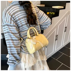 Detail of light yellow Boston bag with pearl lace bow charm and glossy PU leather texture