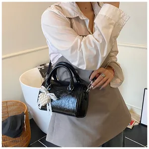 Detail of black mini Boston bag with shiny pleated texture and pearl heart charm accessory