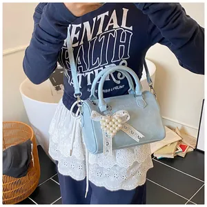 Detail of light blue boston bag featuring a white lace bow and pearl heart charm
