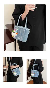 Détail du sac seau en denim bleu clair avec doubles poignées et breloque monstre en peluche