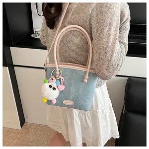 Détail latéral d'un sac seau en jean bleu clair avec poignées roses et accessoire décor