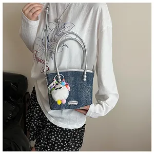 Détail du sac cabas en denim bleu avec bordure argentée et charm poupée en peluche
