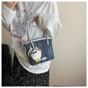 Détail du mini sac cabas en denim bleu avec poignées argentées et breloque peluche