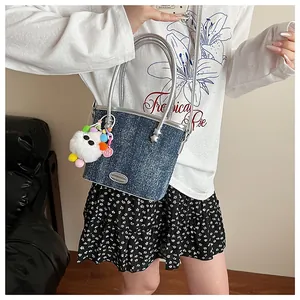 Détail du sac seau en denim bleu foncé avec bordure argentée et breloque peluche sur femme