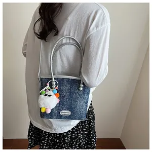 Détail du sac seau en denim bleu avec anses argentées et breloque peluche monstre