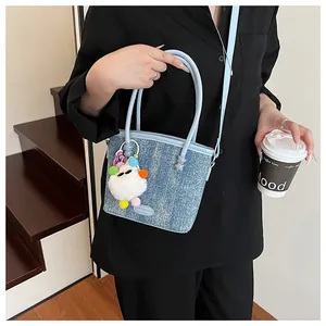 Sac seau en denim bleu avec breloque monstre en peluche blanche porté par un mannequin