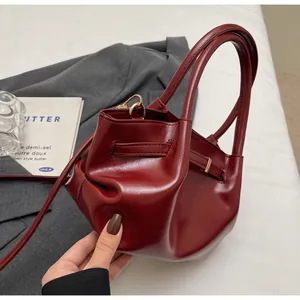 Detailopname van de bordeauxrode lederen emmer-tas met metalen gespen aan de zijkant