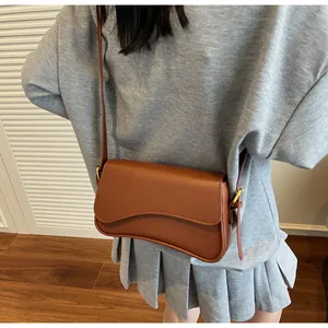 Gros plan d'un sac besace marron en cuir avec rabat ondulé sur tenue décontractée