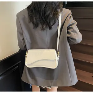Détail du sac selle en cuir blanc cassé avec rabat profilé et boucle dorée sur modèle